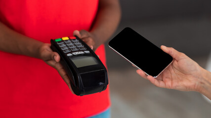 Black delivery man in uniform holding POS machine for payment