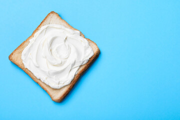 Slice of bread with tasty cream cheese on light blue background, top view. Space for text