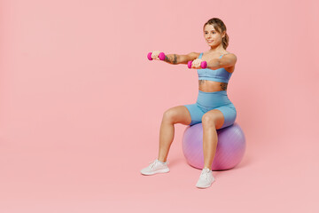 Full body young strong sporty athletic fitness trainer instructor woman wear blue tracksuit spend time in home gym sit on fitball isolated on pastel plain light pink background. Workout sport concept.