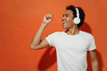 Young black curly man 20s wears white t-shirt listen music in headphones sing song fooling around...