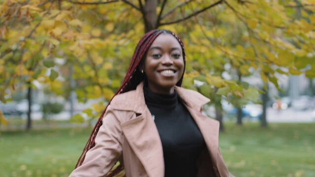 Rear view african american millennial girl model with beautiful long hair stylish hairstyle. Smiling young woman turns back, looks kindly at camera. Portrait pretty lady walking in autumn park alone