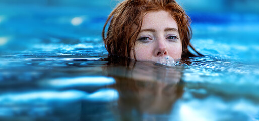 Portrait of young sexy playful woman with red hair, redhead, makes funny bubbles into water with...