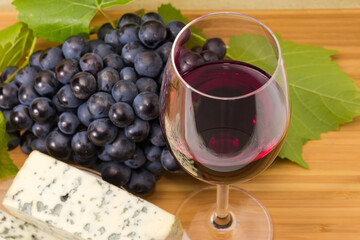 Red wine glass on blurred background of cheese and grapes