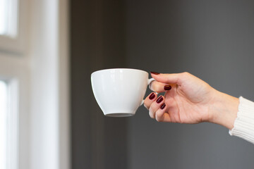 Mockup of female hand holding a coffee cup on office background