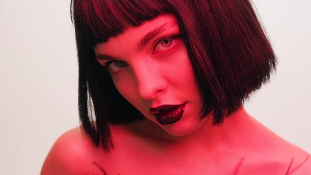 Portrait of a girl in red light with black lips and a wig on a white background in the studio. Woman in neon creative light.
