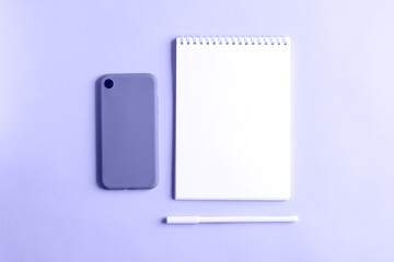 Fototapeta na wymiar An empty notebook, a smartphone in a case, a white pen on a purple background. White page, top view, flat lay. Color concept - very peri color of the year 2022.