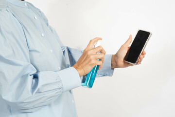 Woman wearing a medical face mask,  spraying disinfectant alcohol on mobile phone, cleaning to eliminate outbreak of Covid-19. Prevent contamination of germs or bacteria infection of  Corona virus.