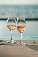 Two glasses of wine  on the edge of infinity swimming pool with panoramic views of the sea at sunset. Drink, celebrate, vacation and summer concept.