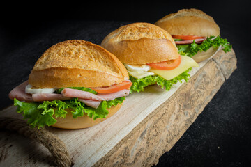Trio of three fresh sandwiches on rustic wooden plank