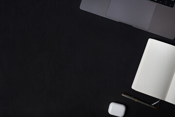 Black desktop with laptop, notepad, pen, letters and headphones