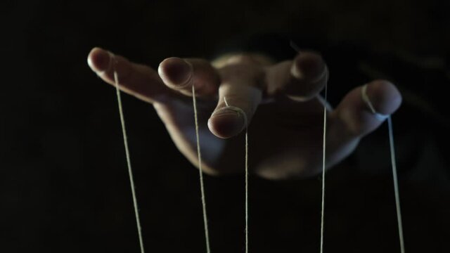 The puppeteer's hand controls the puppets on strings. Manipulation concept