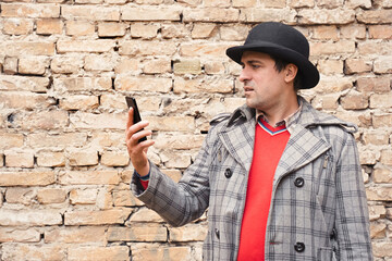 Man with a phone in his hands on a brick wall background.