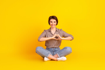 Full body photo of young cheerful girl show fingers heart symbol sit lotus pose isolated over yellow color background