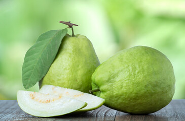 Delicious guava with fresh green leaves on wooden table and green nature background.
