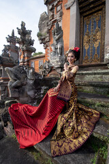 Beautiful balinese girl in traditional costume with a flower and a crown in her hair, and local...