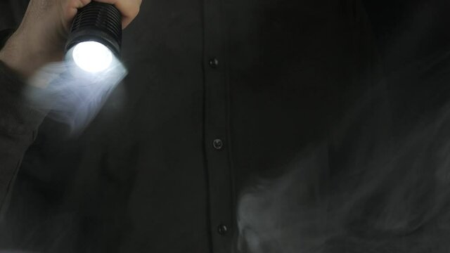 The beam of light from the flashlight moves in complete darkness among the smoke.