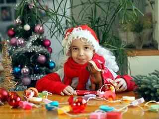 Little girl in Santa Claus hat rejoices and plays with Christmas balls and a toy dog. Eve meeting Christmas or New Year.