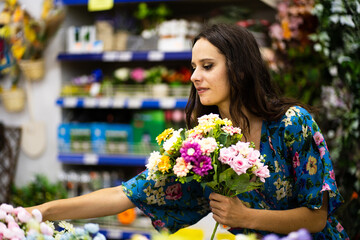 Woman choosing flowers to buy from a bucket in a florist shop