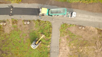 Asphaltfertiger, Teermaschine und Lastkraftwagen asphaltieren eine Baustraße zur Erschließung...