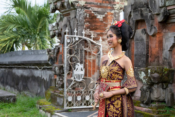 Young Balinese girl in traditional dress with a flower in hair, ocal temple in Bali, Indonesia.