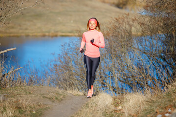 Young woman jogging in the park near the pond in the cold sunny morning. Sporty girl running in countryside