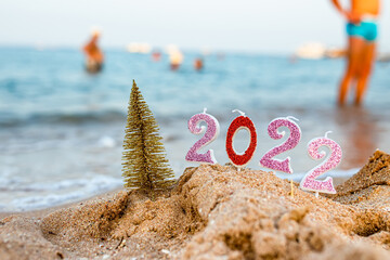 Figures 2022 with Christmas tree against background of coastal waves by ocean or sea with caramel...