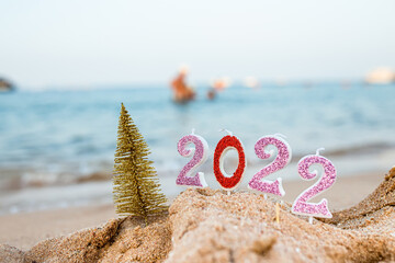 Figures 2022 with Christmas tree against background of coastal waves by ocean or sea with caramel cane. Travel during quarantine on New Year's Eve against the background of people swimming in the sea