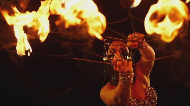 Young woman dancing performing cool and dangerous fire show and doing many tricks with fire . Dressed in black with mask closed half of face . Burning iron fire wings at night. Asian , Arabian culture