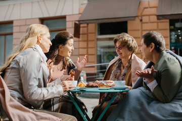 A group of older friends sit in a cafe on the terrace, drinking coffee and talking.