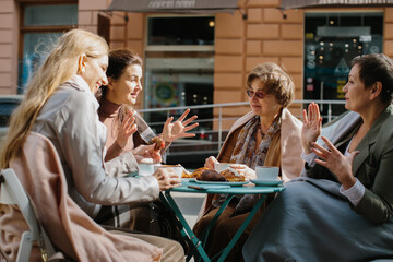 A group of older friends sit in a cafe on the terrace, drinking coffee and talking.