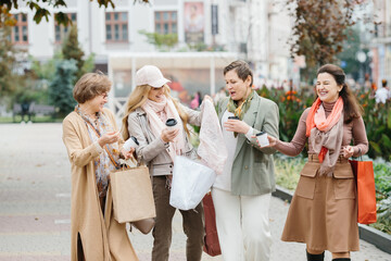 A group of smiling adult women holding shopping bags while walking through the city