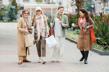 A group of smiling adult women holding shopping bags while walking through the city