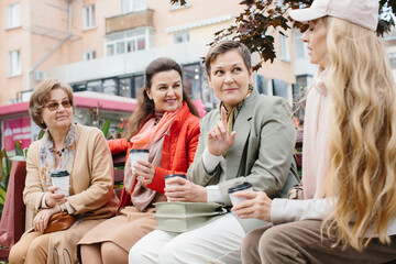 Senior women friends with coffee sitting outdoors on terrace, resting.
