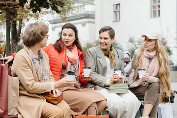Senior women friends with coffee sitting outdoors on terrace, resting.