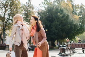 Senior female girlfriends discussing shopping while walking the city streets.