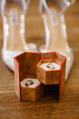Elegant beautiful white shoes of the bride on the background Wedding accessories Brown rings box with two gold rings standing on the table Bridal morning concept Cropped photo Close up