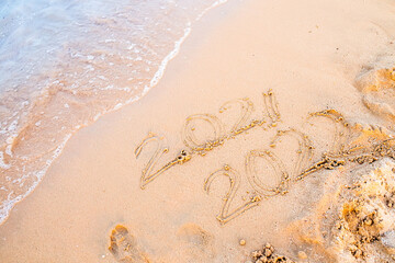 Message Year 2021 replaced by 2022 written on beach sand background. New Year 2021 is coming concept. Background for New Year's banner or advertising
