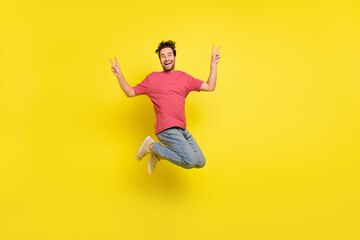 Fototapeta na wymiar Full size photo of impressed brunet young guy jump show v-sign wear t-shirt jeans sneakers isolated on yellow background