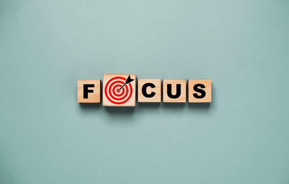 Top view or flat lay design of focus wording on wooden cube block with red dartboard and arrow drawing for concentrate with business objective target concept.