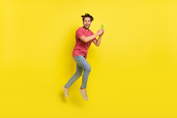 Fototapeta na wymiar Full body profile photo of cool beard young guy run hold telephone wear red t-shirt jeans footwear isolated on yellow background