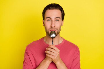 Photo of positive funny guy lick spoon enjoy delicious meal wear pink t-shirt isolated yellow color background - obrazy, fototapety, plakaty