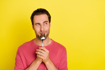 Photo of curious dreamy guy lick spoon look empty space wear pink t-shirt isolated yellow color...