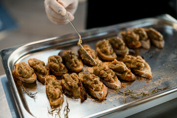 hand of chef spreads by spoon the vegetable blend on slices of baguette on tray