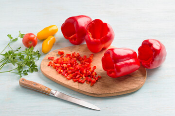 Wooden board with chopped red bell peppers, whole peeled bell peppers, tomatoes and parsley on a...
