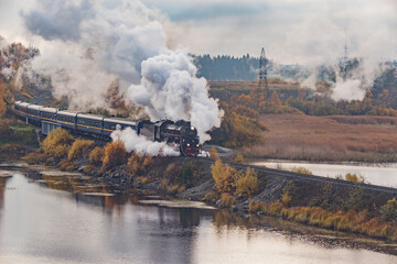 Retro steam train moves along the lake at autumn cloudy morning. Republic of Karelia.