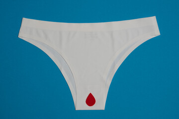White female underwear with  red artificial drop of blood, isolated on blue background.