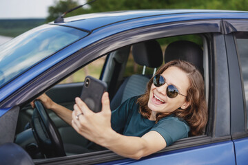 Fototapeta na wymiar Beautiful young woman in sunglasses smiling communicating video call using smartphone while sitting in car