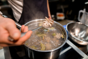 selective focus on small boiled octopus in a spoon over pot of boiling water