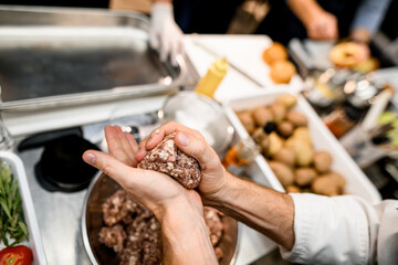 hands of the man hold a piece of minced meat and form a cutlet