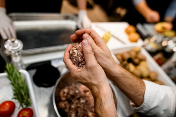 hands of the man hold a piece of minced meat and skilfully form a cutlet